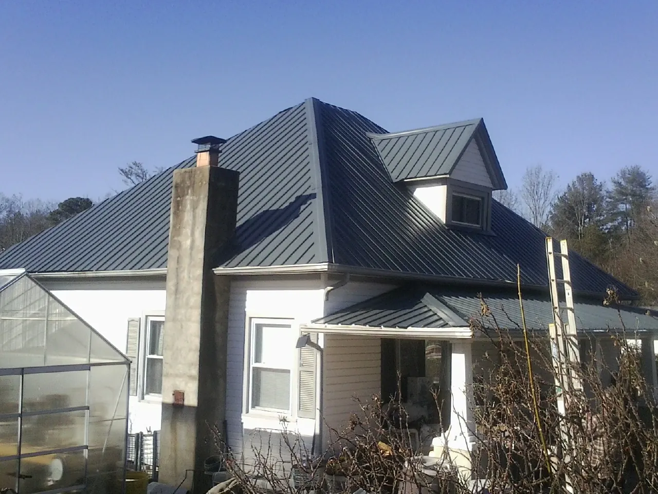 Dark blue standing seam metal roof on a white farmhouse with dormer — Slate & Tile Roof Repair by Roofing Brothers in Port Gibson