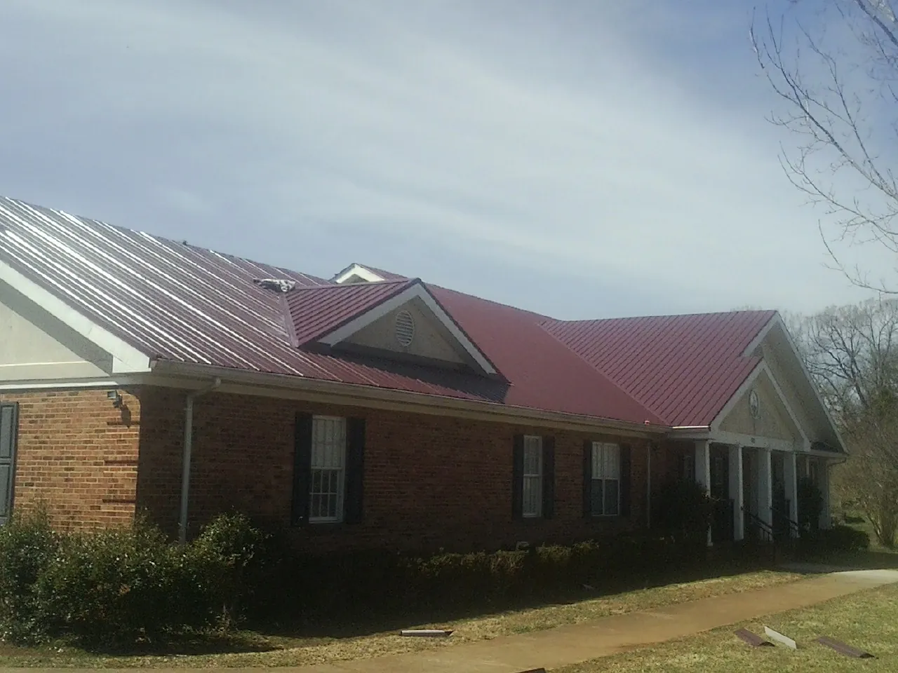 Red metal roof with gabled entries on a long brick building, from a Hail Damage Roof Repair job in Port Gibson