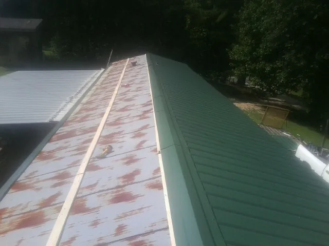 Old rusted panels beside newly installed green metal roofing — Wind Damage Roof Repair by Roofing Brothers in Port Gibson