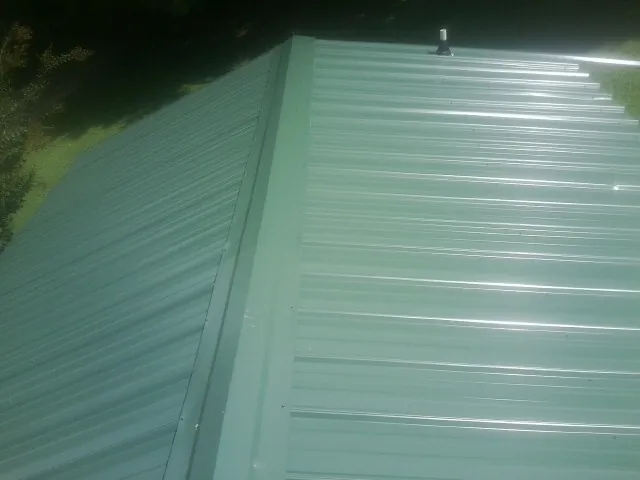 New green metal panels meeting at the ridge of a roof — Flat Roof Repair work by our crew in Port Gibson