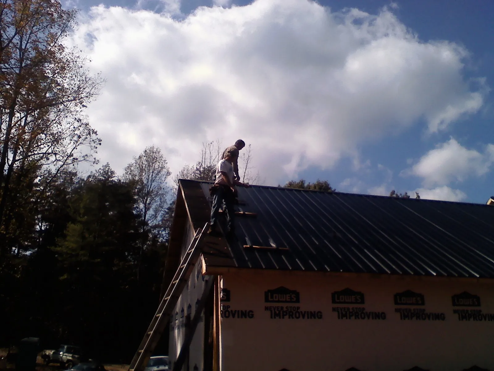Roofer fastening dark metal panels high against a cloudy sky, from a Roof Inspection job in Port Gibson