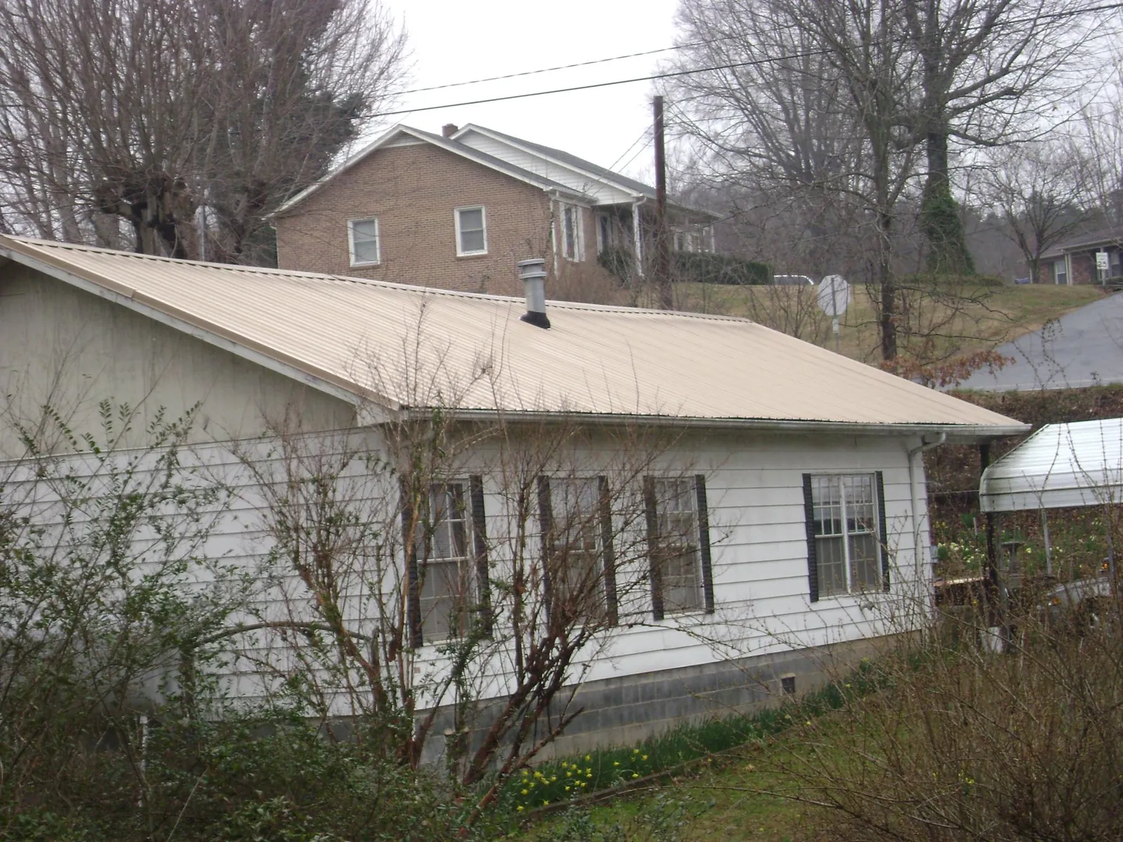 Tan metal roof on a white sided house set into a hillside — Commercial Roofing by Roofing Brothers in Port Gibson