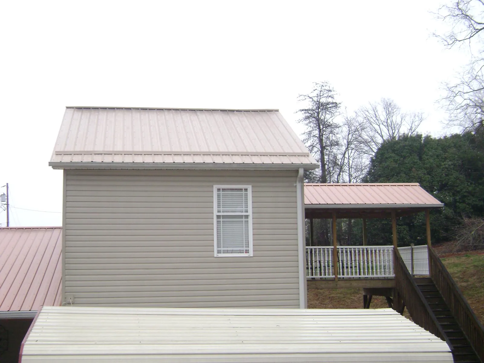 Tan metal roofs on a two story addition and attached porch, from a Roof Replacement job in Port Gibson